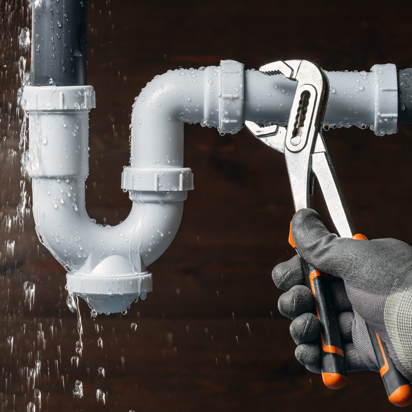 Close up of a plumber hand fixing a water leak in a sink drain siphon pipe with an adjustable pliers. Home insurance for emergency plumbing breakdowns repair.